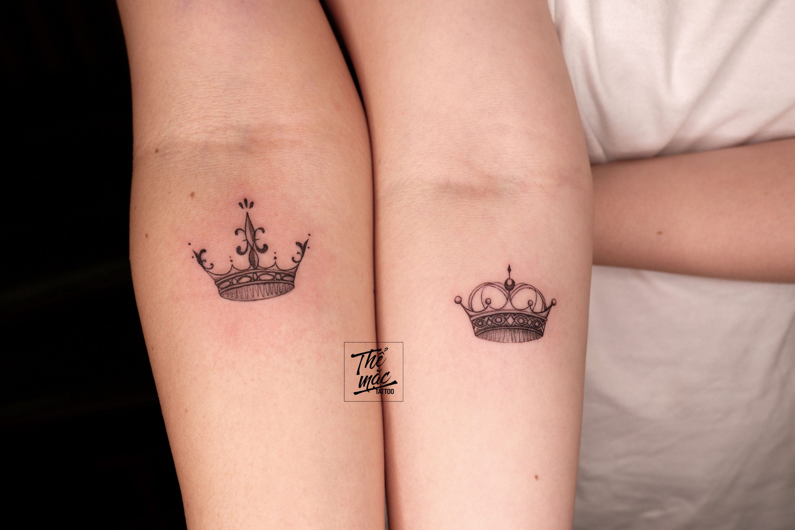 A pair of matching crown tattoos on two forearms, each with unique designs — symbolizing friendship, royalty, or sisterhood.