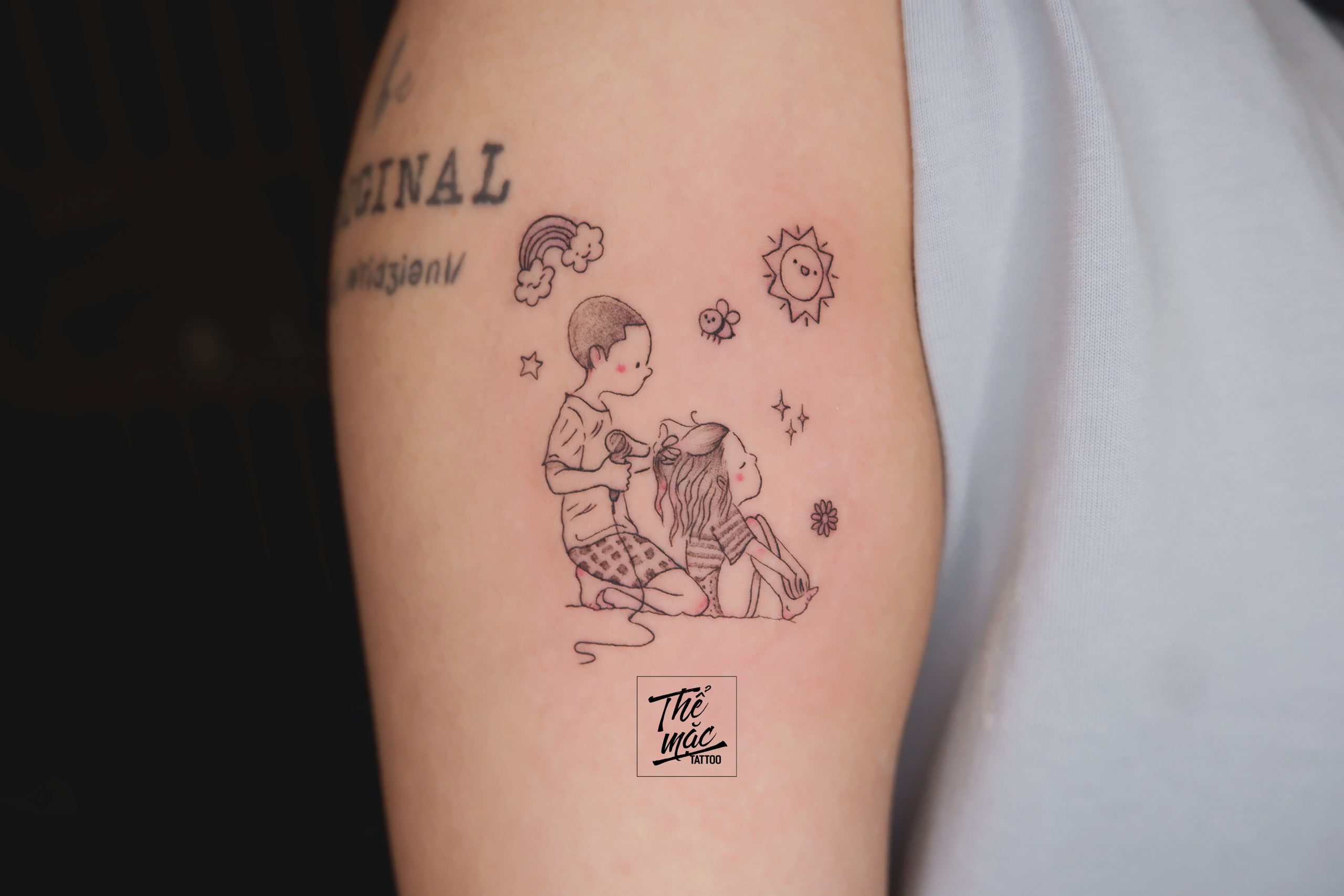 Fine line tattoo of two children playing under sun, stars, and rainbow – a whimsical, nostalgic design created at Thể Mặc Tattoo, Ho Chi Minh City.