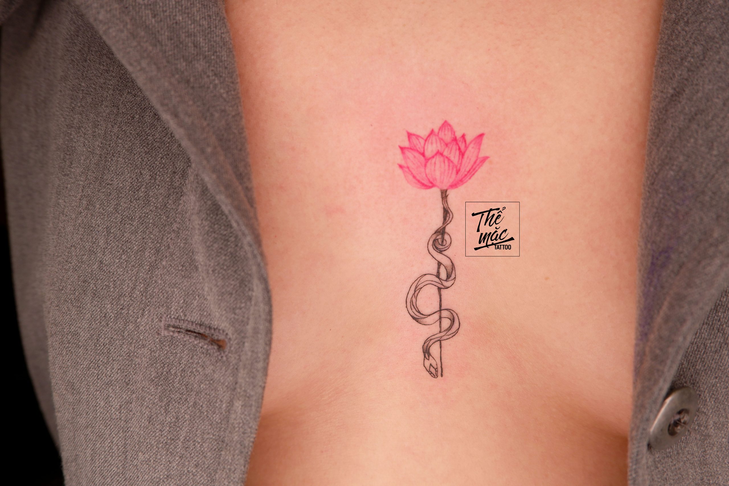 Lotus and snake fine line tattoo – a graceful blend of floral and animal symbolism, crafted in minimalist detail by Thể Mặc Tattoo.