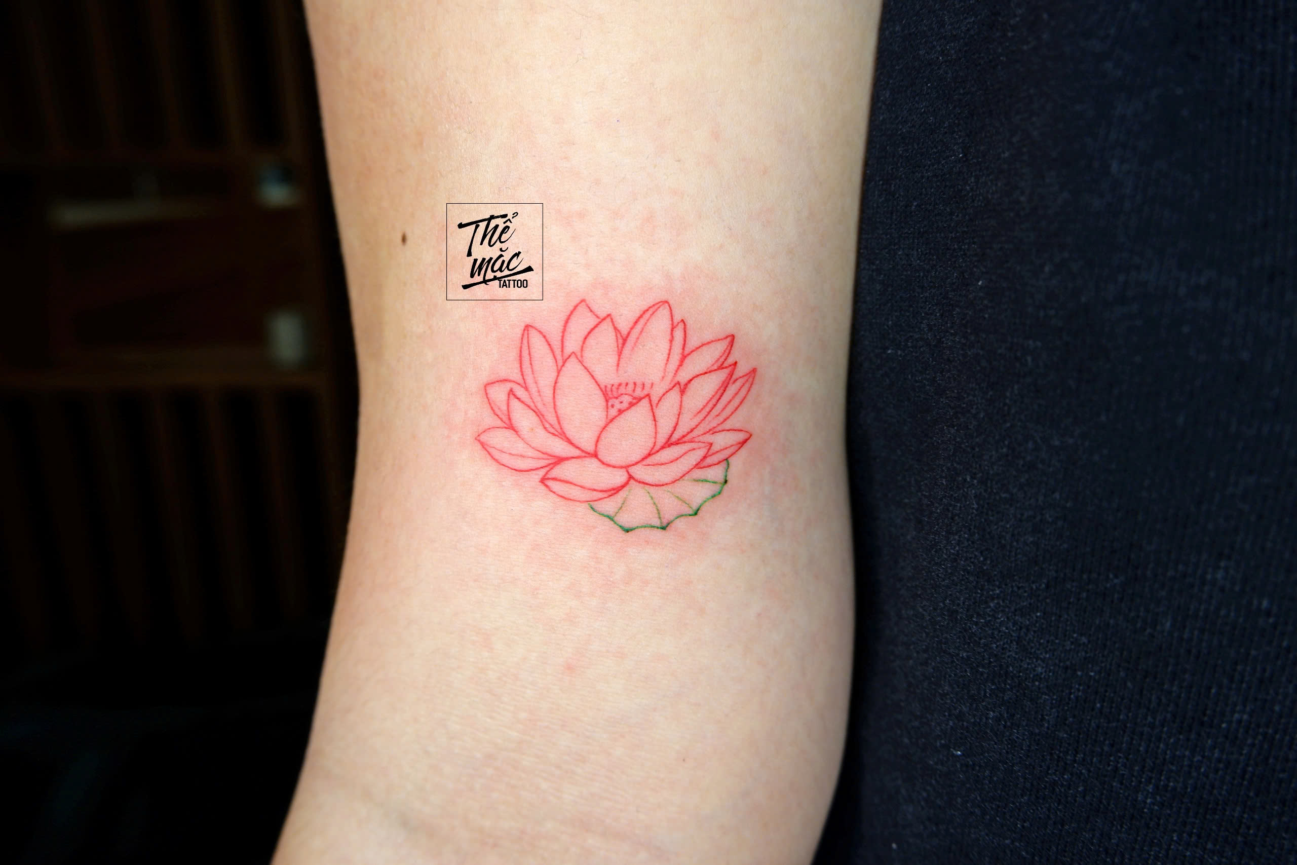 Red lotus flower linework tattoo with subtle color details, inked by custom tattoo studio in Saigon.