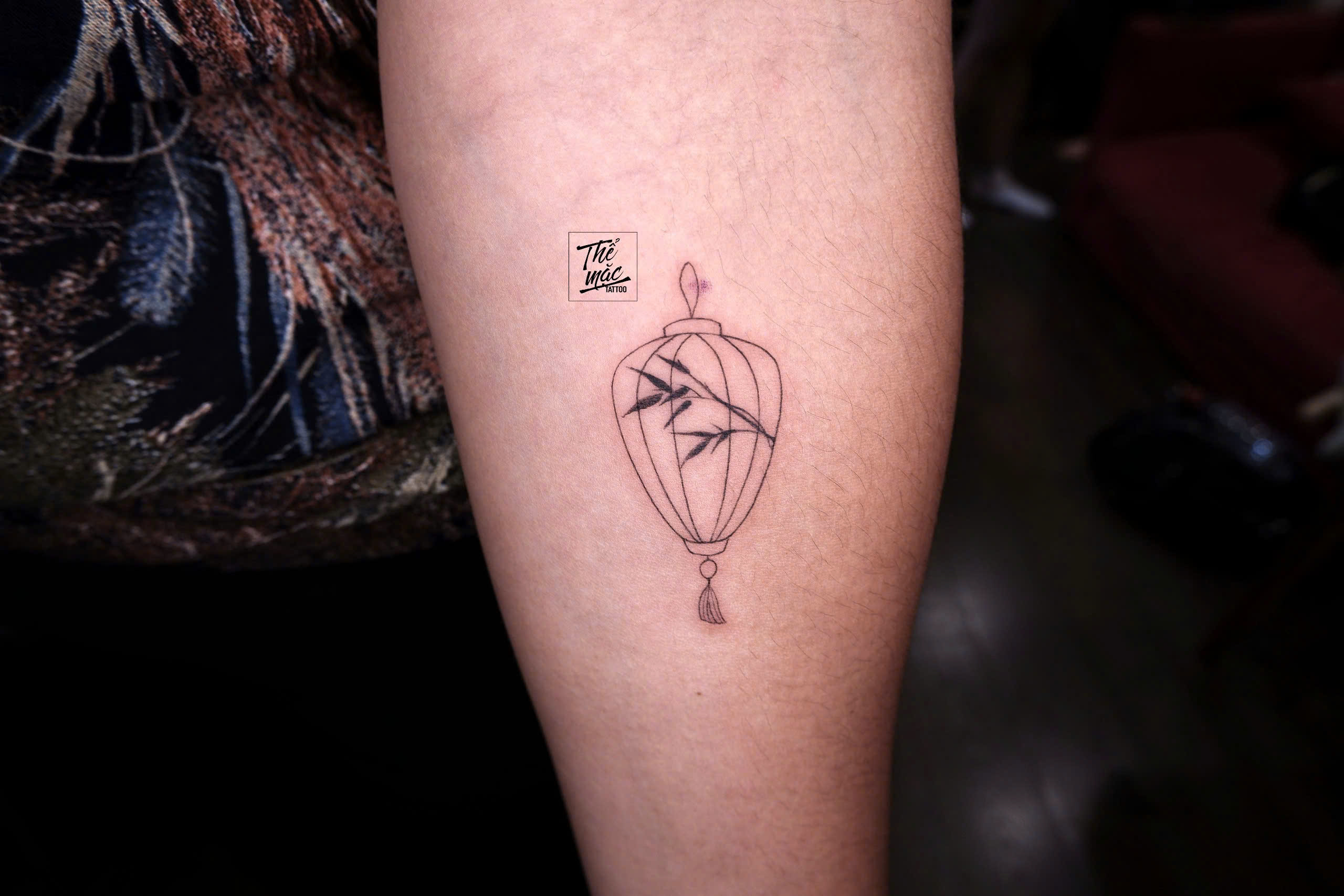 Traditional lantern fine line tattoo with bamboo leaves, designed by female tattoo artist in Ho Chi Minh City.