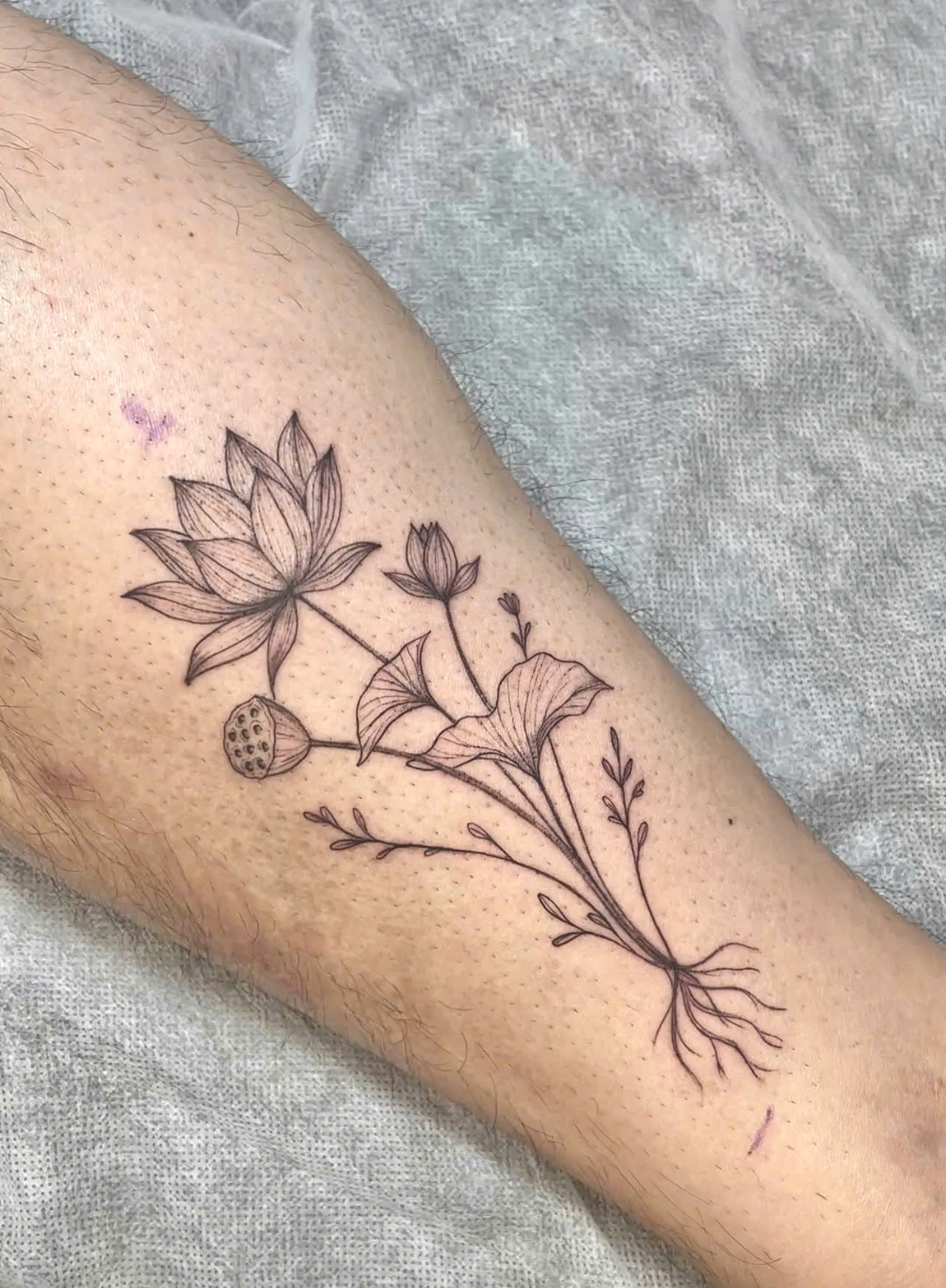 Delicate lotus flower fine line tattoo on calf, designed by custom tattoo artist in Saigon.